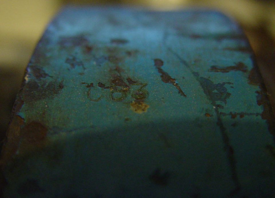 Close-up of a blue metal part with numbers '2802' stamped into it. Some rust is visible