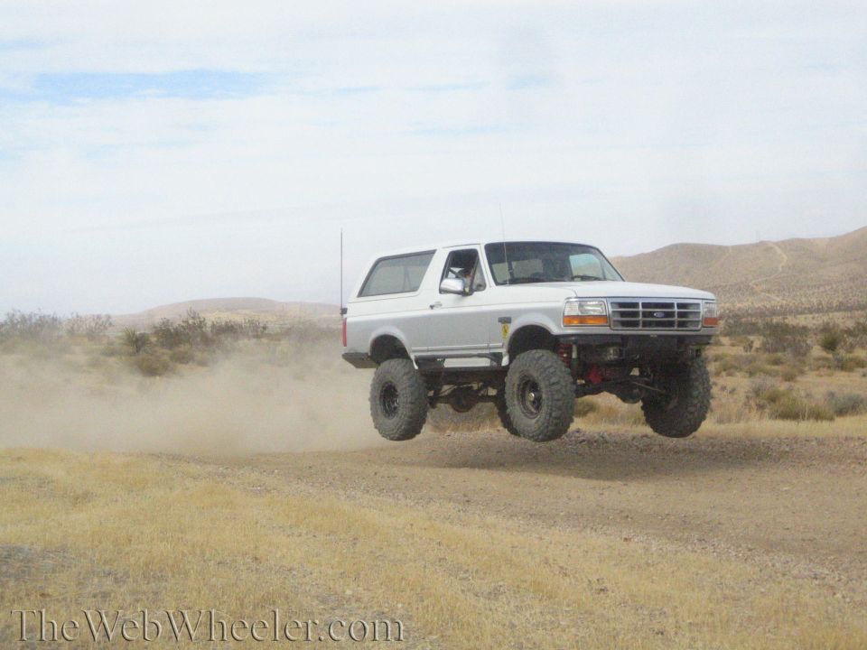 White lifted Ford Bronco jumping with wheels off a desert road