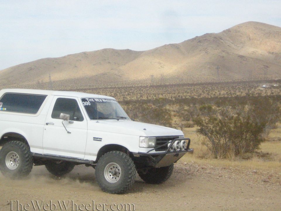 White lifted Bronco-style SUV on a desert dirt road below tan hills
