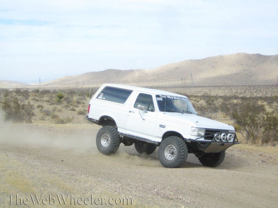 White lifted Bronco-style SUV cornering on a desert dirt road