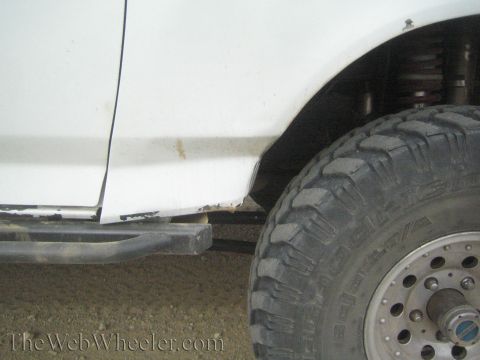 1990 Ford Bronco - Close-up of a white truck's lower body, dented tube rocker step bar, and a chunky mud-terrain tire.