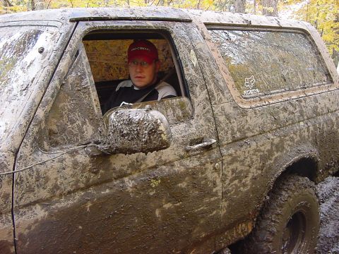 1994 Ford Bronco - A mud-caked Ford Bronco navigates a challenging off-road terrain.