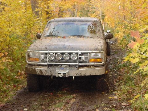 1994 Ford Bronco - Muddy 1994 Ford Bronco navigates a dirt path surrounded by autumn trees.