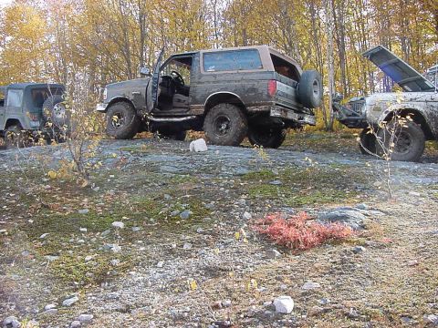 1994 Ford Bronco - Several off-road vehicles are parked on a rocky, wooded area during autumn.