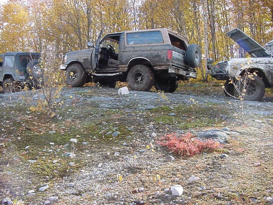 Mud-covered dark green Ford Bronco with doors open, parked on rocky terrain