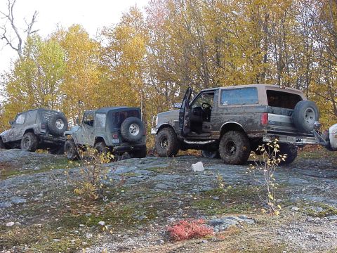 1994 Ford Bronco - A 1994 Ford Bronco is parked on rocky terrain alongside other off-road vehicles, with its doors open.