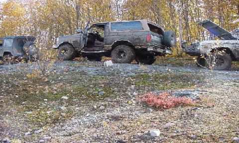 1994 Ford Bronco - Three muddy SUVs are parked on a rocky, wooded area during autumn.