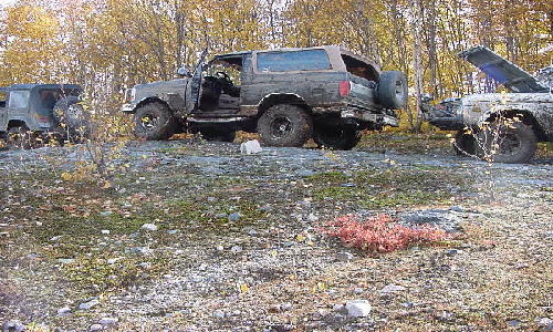 Mud-covered 1980s Ford Bronco with doors open, parked on a rocky incline