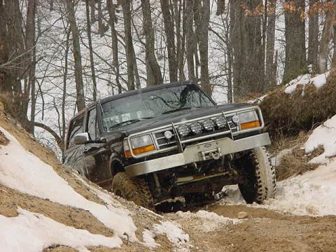 1994 Ford Bronco - A black 1994 Ford Bronco navigates a snowy, off-road trail with trees in the background.