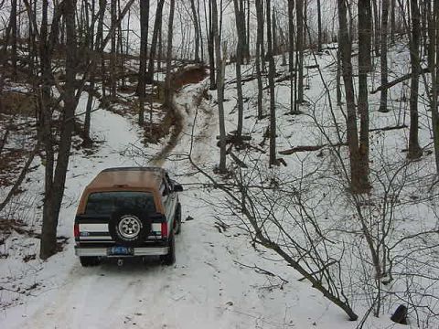 1994 Ford Bronco - 1994 Ford Bronco navigates a snow-covered path through a wooded area.
