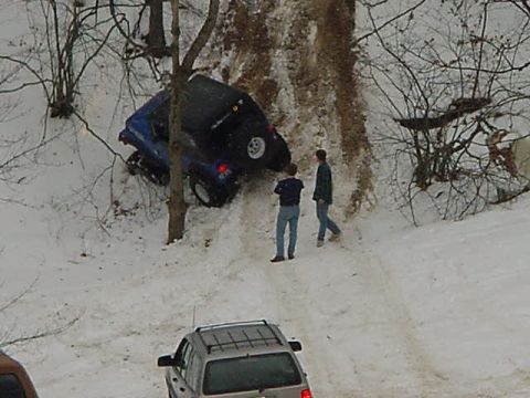 1994 Ford Bronco - Two people watch a blue SUV stuck on a snow-covered hill, with another vehicle visible below.