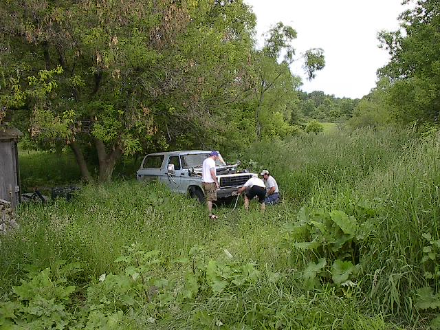 1978 Ford Bronco in tall grass with two people working on the front bumper