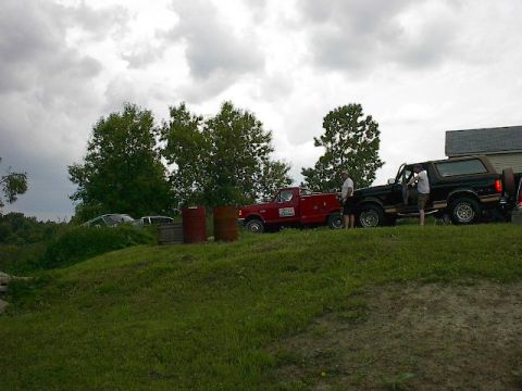 1994 Ford Bronco - A black 1994 Ford Bronco with a brown top is parked next to a red truck on a grassy hill.