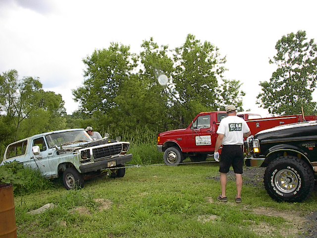 Light blue SUV with hood open, being towed by a red truck. The SUV's front end is damaged