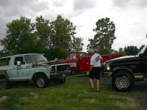 1994 Ford Bronco - A light blue Ford Bronco from the late 1970s is being towed by a black truck, with a red truck visible in the background.