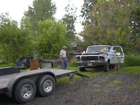 1994 Ford Bronco - A person works on an old pickup truck with its hood open, while a trailer sits nearby.