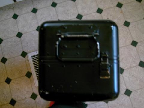 1986 Ford Bronco - A black metal box with a handle and latch sits on a tiled floor next to a vent.