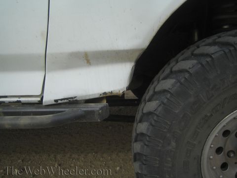 1990 Ford Bronco - Close-up of a white truck's lower body panel, tube step bar, and a deep-lug mud-terrain tire.