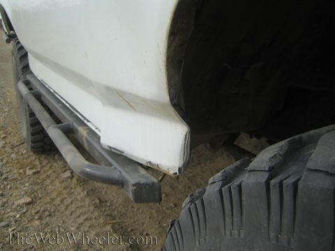 1990 Ford Bronco - Close-up of a scuffed white truck rocker panel and lower body above a tubular rock-slider step, with a chunky mud-terrain tire in the foreg…