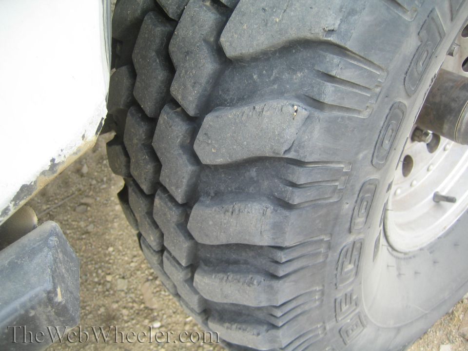 Close-up of a large aggressive mud-terrain tire on a steel wheel beside a white truck