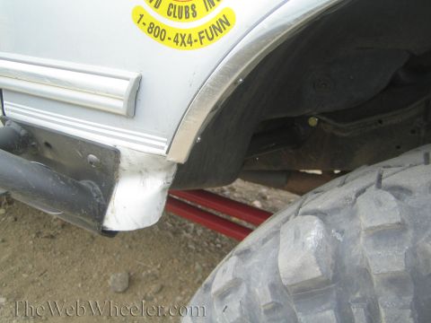 1990 Ford Bronco - Rear lower body of a lifted white truck showing a yellow club decal reading 1-800-4X4-FUNN, with a red jack stand and large off-road tire b…