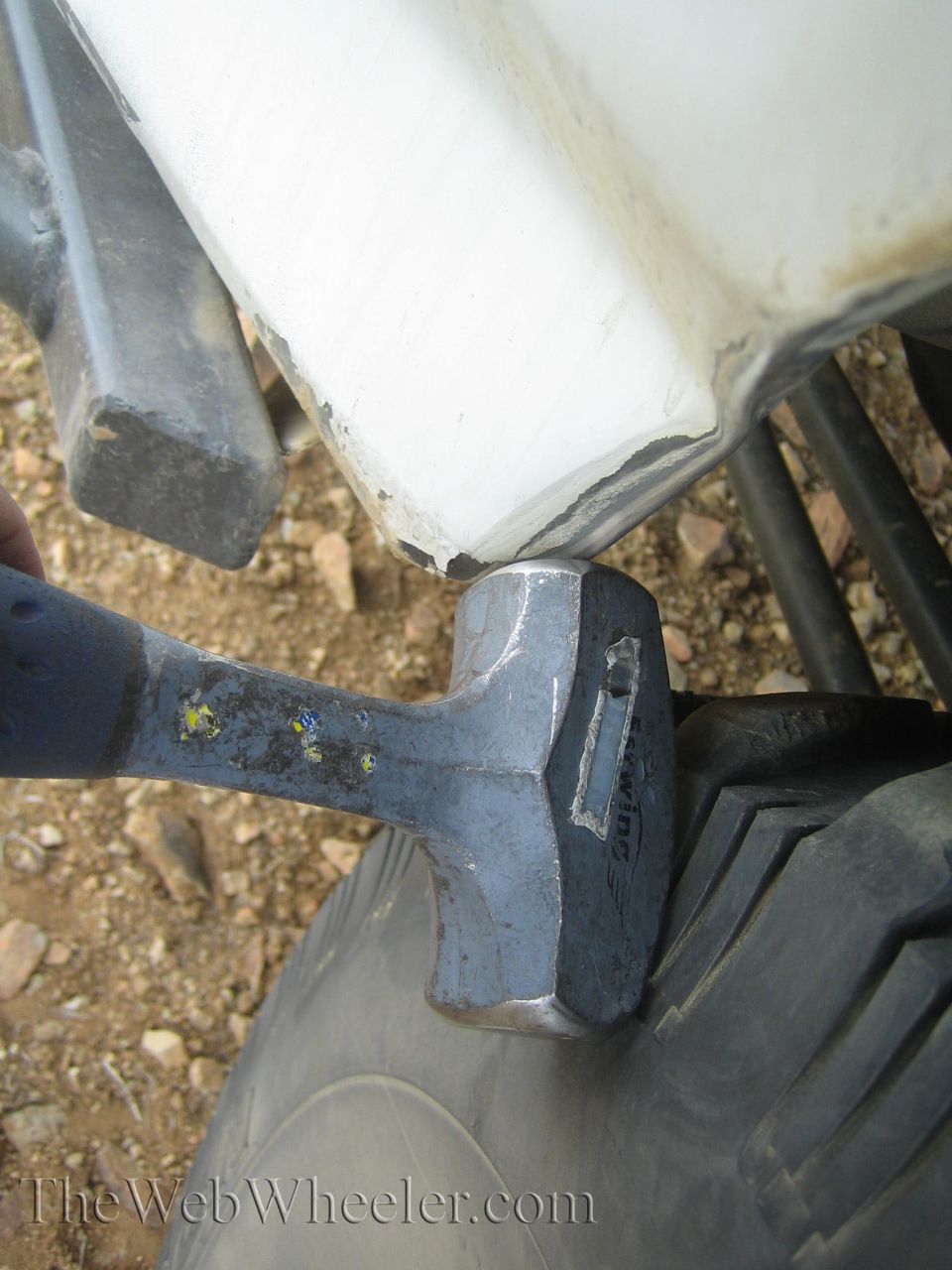 Sledgehammer resting against a damaged white truck body panel on the trail