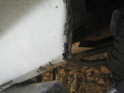 1990 Ford Bronco - Close-up of a broken, jagged corner of a white truck body panel revealing damage above the suspension and a tire.