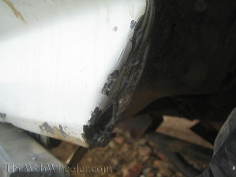 1990 Ford Bronco - Close-up of a cracked white truck body panel with a crumbling damaged corner, set above rocky trail ground.