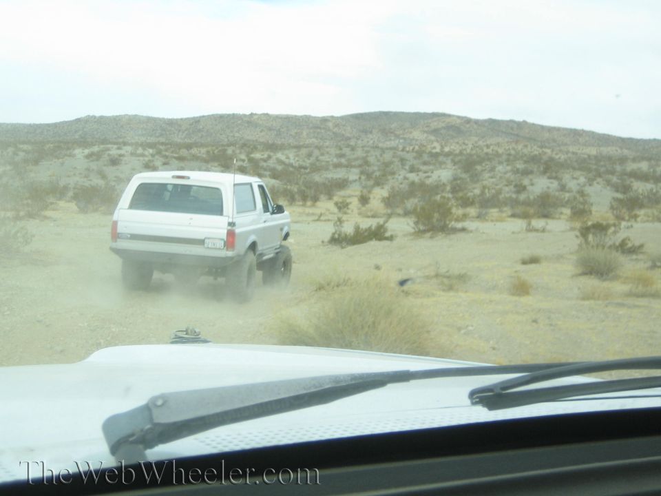 White SUV driving on a desert trail seen through a windshield with wiper