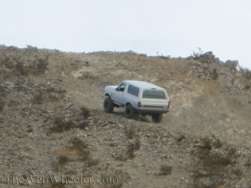 Light gray SUV cresting a rocky desert ridge during a hillclimb