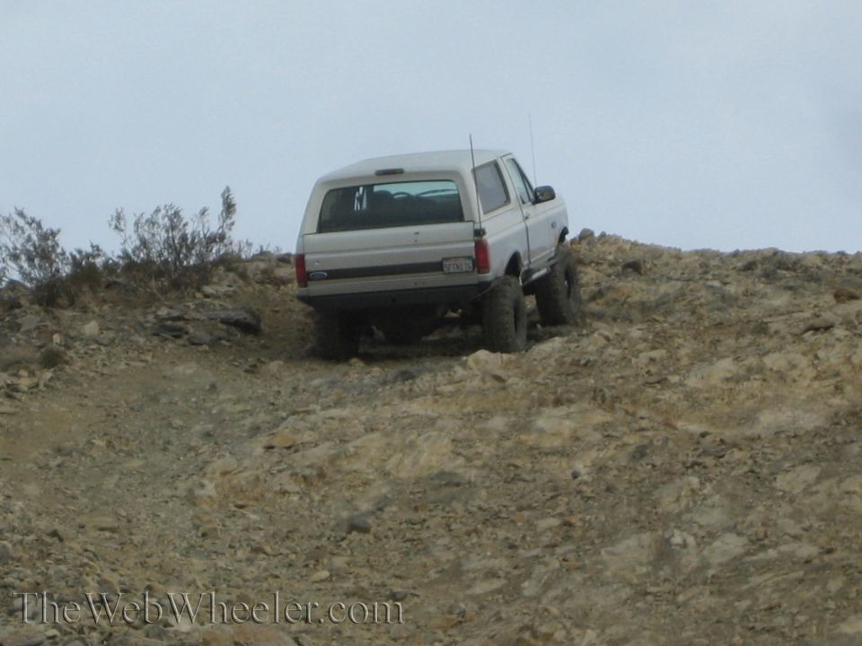 White Ford Bronco SUV climbing a rocky hill, Ford tailgate badge visible