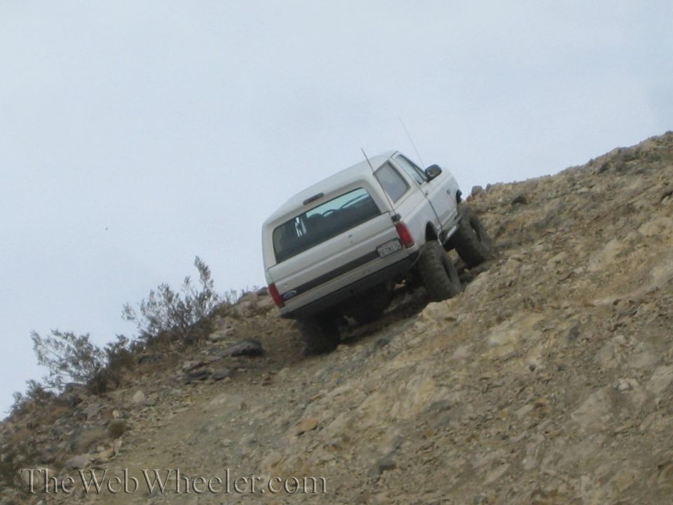 White SUV tilted heavily while climbing a steep rocky off-road slope