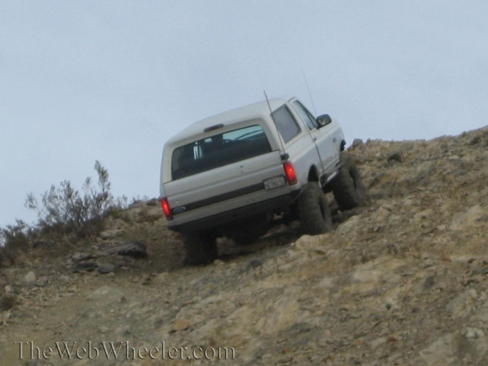 Rear view of silver lifted SUV climbing a rocky off-road incline