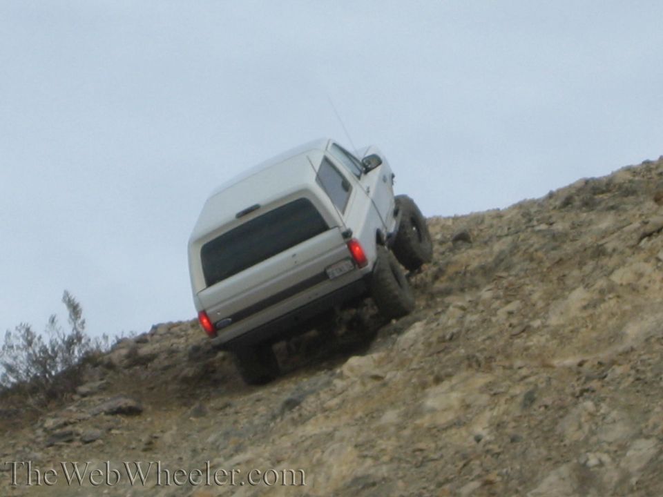 Silver SUV angled steeply on a rocky off-road hill, rear tail lights lit