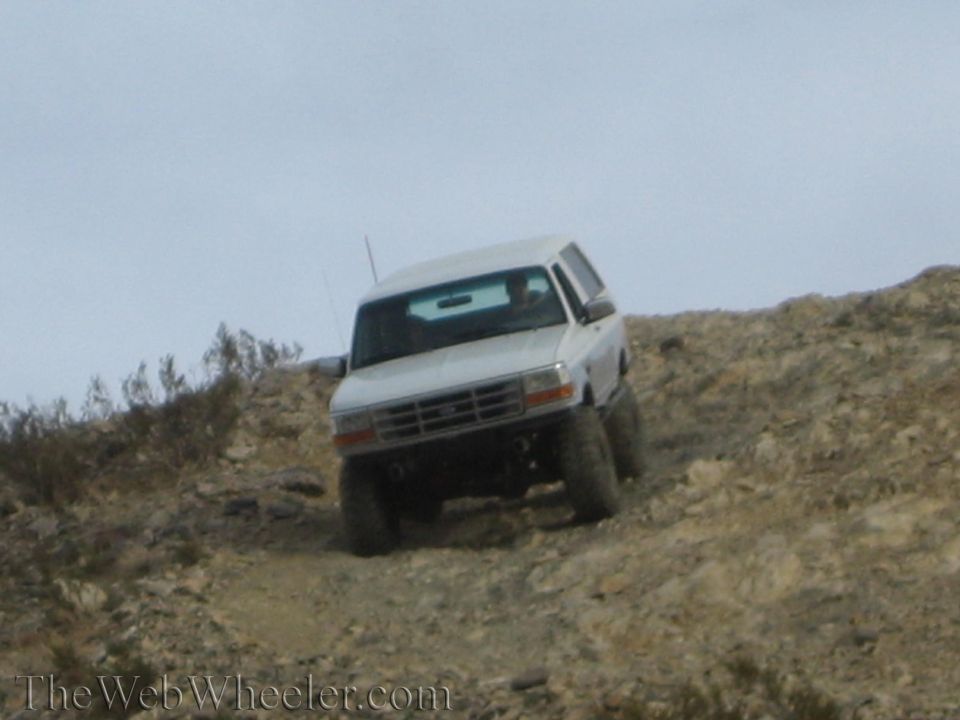 Front view of white Ford SUV climbing a rocky off-road dirt hill