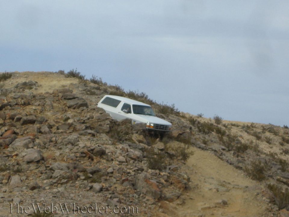 White SUV descending a steep rocky desert slope on a dirt trail