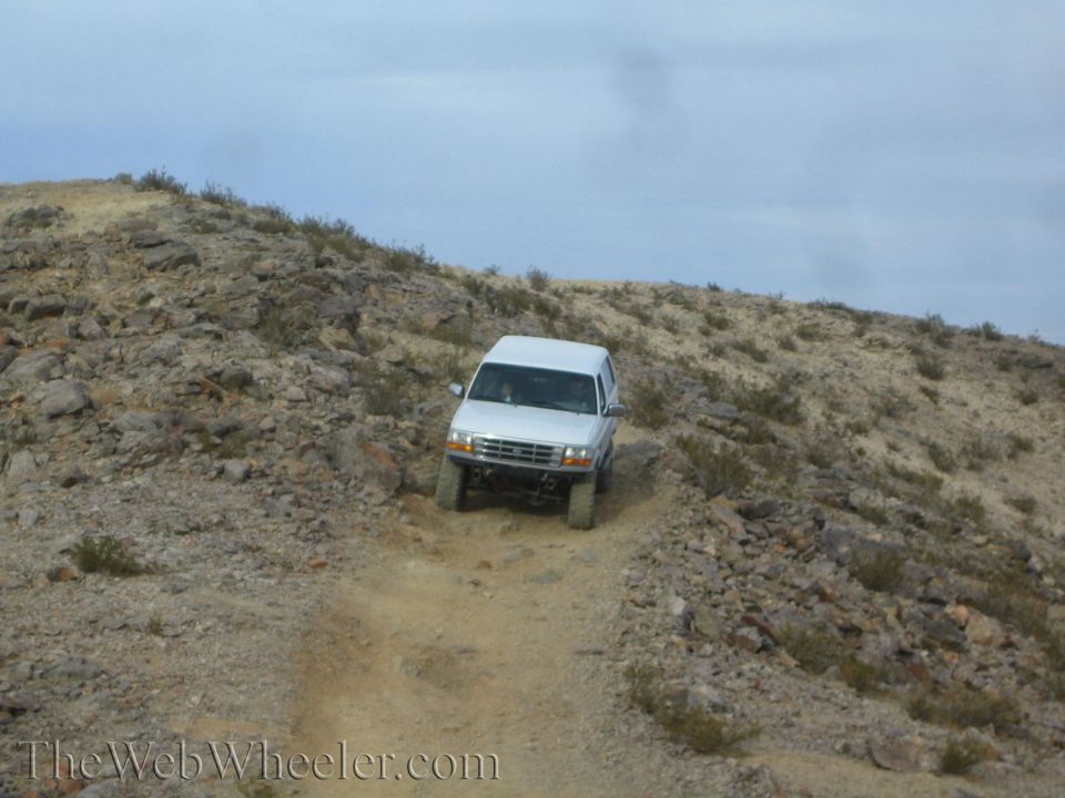 White SUV climbing a sandy rutted trail up a rocky desert hill