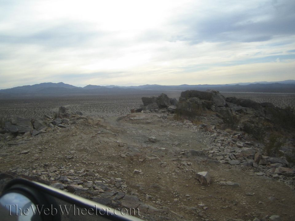 View over a rocky ridge across a vast desert valley toward distant mountains