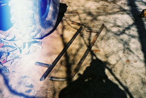 1978 Ford Bronco - Scanned film photo of two shop-fabricated bare-steel tube side bars laid out on a shaded concrete driveway. A mud-terrain tire on a chrome…