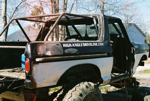 1978 Ford Bronco - A stripped early Ford Bronco with a black upper body and light gray lower panels, fitted with a welded tubular roll cage and lifted on larg…