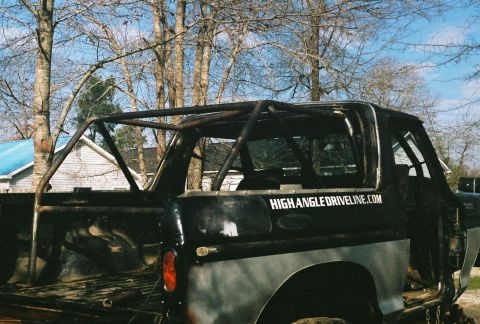 1978 Ford Bronco - Black full-size Ford Bronco with its hardtop removed to reveal a bolted-in multi-point roll cage; the rear quarter is bare gray metal and t…