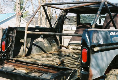 1978 Ford Bronco - Looking into the open rear of a topless full-size 4x4 with a welded multi-point roll cage, bare diamond-plate cargo floor, tailgate dropped…