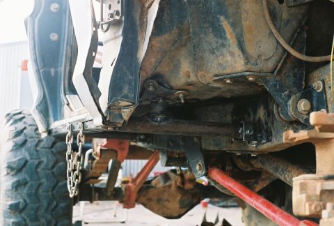 1978 Ford Bronco - Low-angle underbody shot of a lifted 4x4 on jack stands in a shop, looking along the frame rail at the transmission and transfer case, grea…