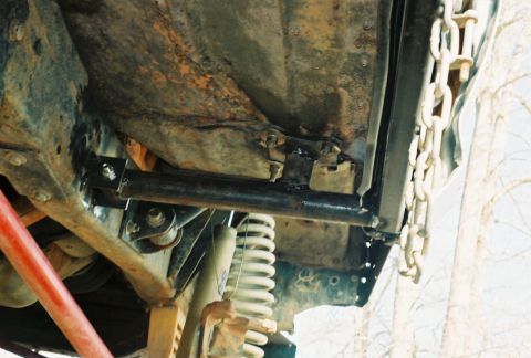 1978 Ford Bronco - Film photo taken from underneath a truck looking up at a rusty floor pan and frame rail, with a black steel tube crossmember bolted to weld…