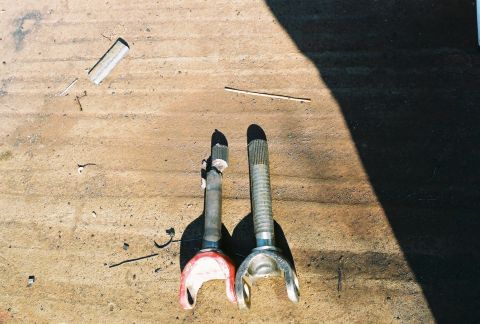 1978 Ford Bronco - Two axle shafts are shown side-by-side on a rough surface, with a shadow cast from the right.