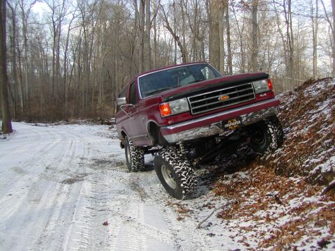 1991 Ford Bronco - A red 1991 Ford Bronco navigates a snowy incline in a forest setting.