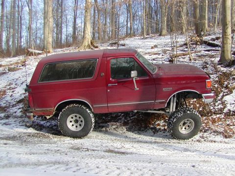 1991 Ford Bronco - A red 1991 Ford Bronco is shown with a lifted suspension, parked in a wooded area with snow on the ground.