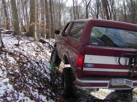 1991 Ford Bronco - 1991 Ford Bronco navigates a snowy, wooded path with its tires on the incline.