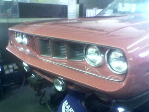 1988 Ford Bronco - The front grille and quad headlights of a pink 1970 Plymouth Barracuda are visible.