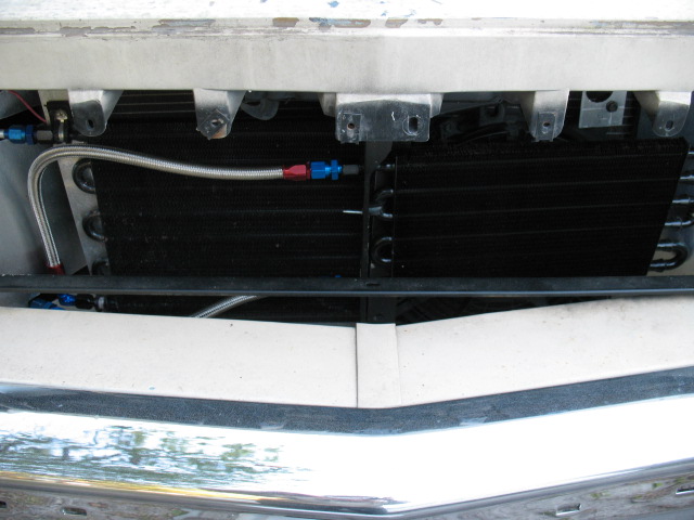 Close-up of an aftermarket oil cooler mounted in front of a radiator, with braided lines and blue/red fittings